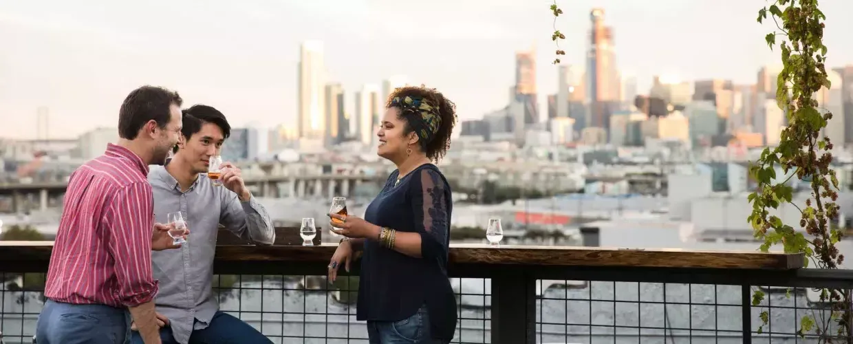 Three people gather around an outdoor table on the roof deck of Anchor Distilling in 威尼斯人官网平台app，加利福尼亚.